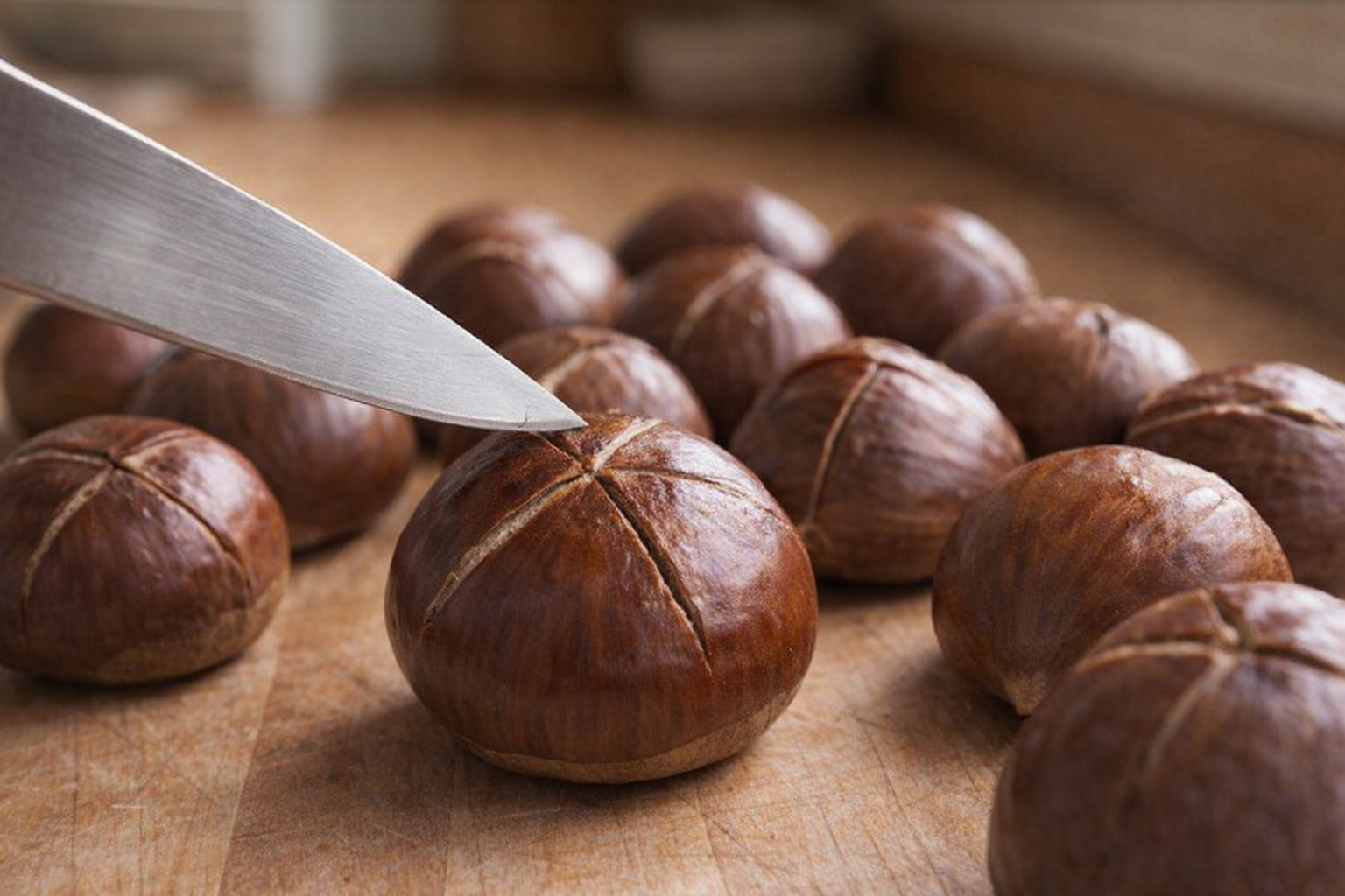 Close-up shot of raw chestnuts on a wooden cutting board, one being scored with a sharp knife, good lighting highlighting the chestnut's texture